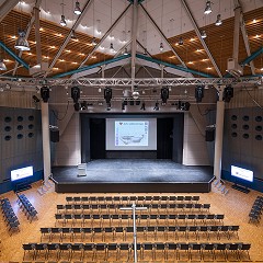 Großer Saal verdunkelt mit Beleuchtung in maximaler Reihenbestuhlung mit Bühnenfrontansicht, Saal abgestuft